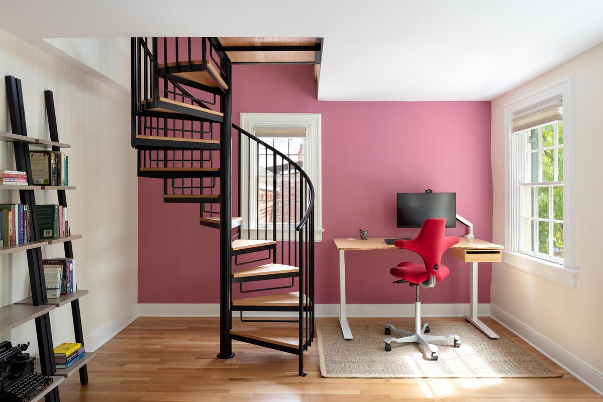 Four Brothers Design + Build home office renovation in Georgetown, Washington, DC, featuring a black spiral staircase, pink accent wall, built-in desk, and modern shelving.