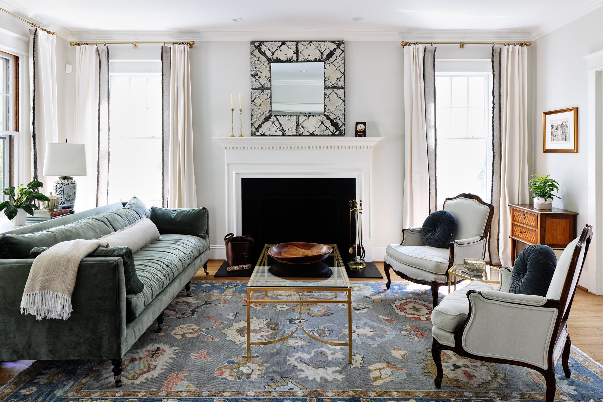 Living room in a Massachusetts Heights, DC, home renovated by Four Brothers Design + Build, with a white fireplace mantel flanked by tall windows and a green sofa. Living room in a Massachusetts Heights, DC, home renovated by Four Brothers Design + Build, with a white fireplace mantel flanked by tall windows and a green sofa.