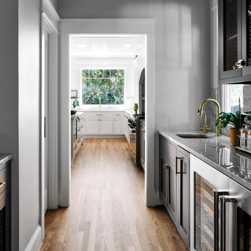 Butler’s pantry by Four Brothers Design + Build in Massachusetts Heights, DC, with dark cabinetry and beverage refrigerators along a passage to the kitchen.