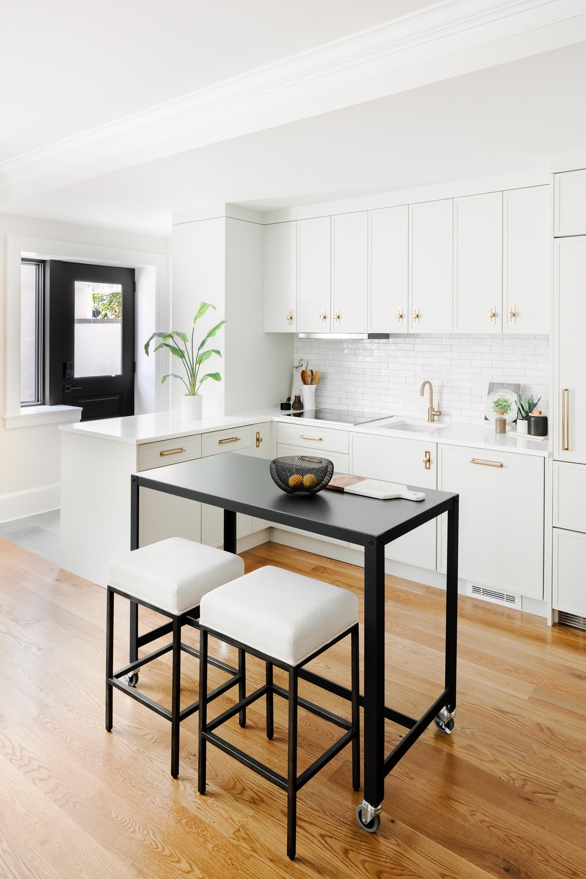 White kitchen by Four Brothers Design + Build in a Logan Circle, DC, row home, featuring a subway tile backsplash and two upholstered stools at a rolling island.